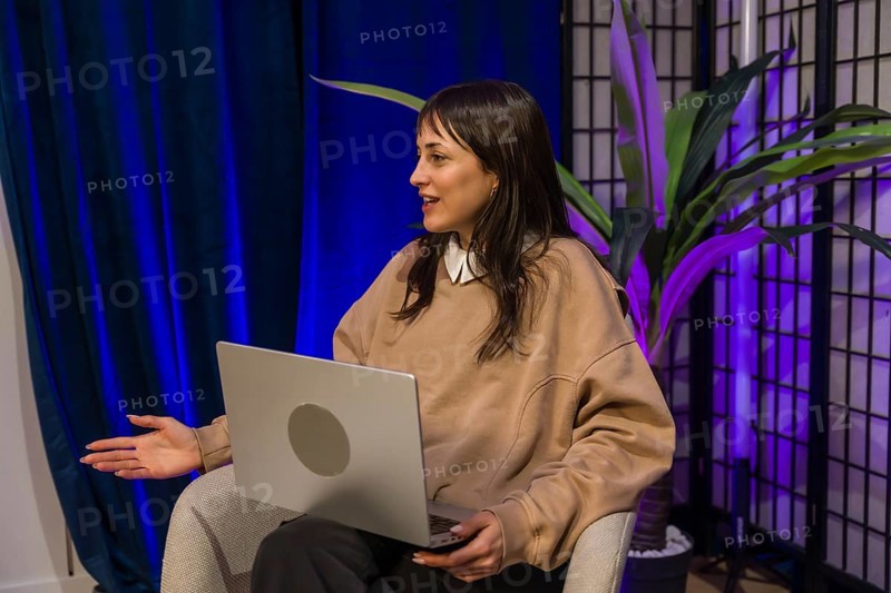 Woman presenting ideas from a modern content creation studio, smiling and gesturing while recording a podcast or livestream with laptop and professional lighting setup