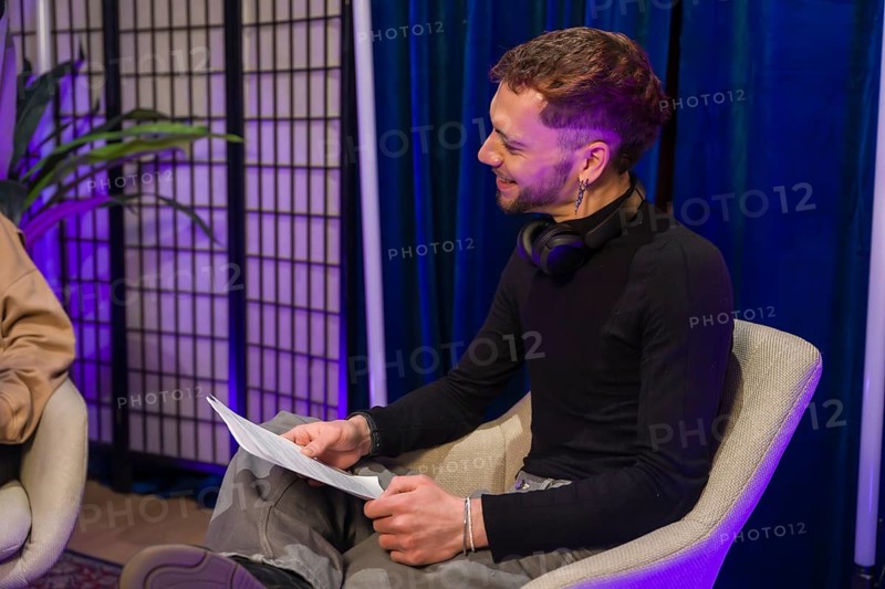 Man in a modern studio setting holding notes and smiling while recording a podcast or creating social media content, focusing on communication and digital media production