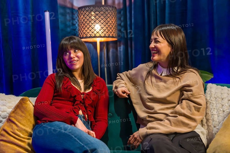 Two cheerful young women are having a conversation and laughing while creating content for a podcast or social media in a modern studio setup with vibrant lighting