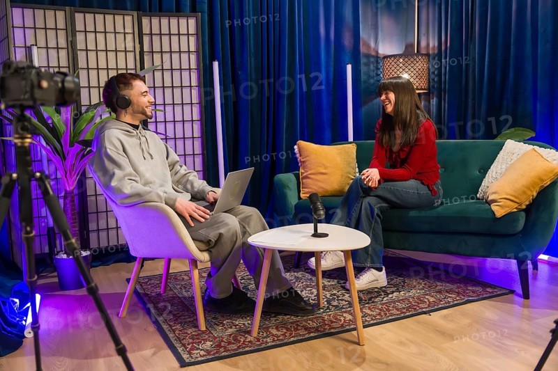 Diverse young content creators recording a podcast or social media video, sitting in a modern studio setup with microphone, laptop, and camera equipment