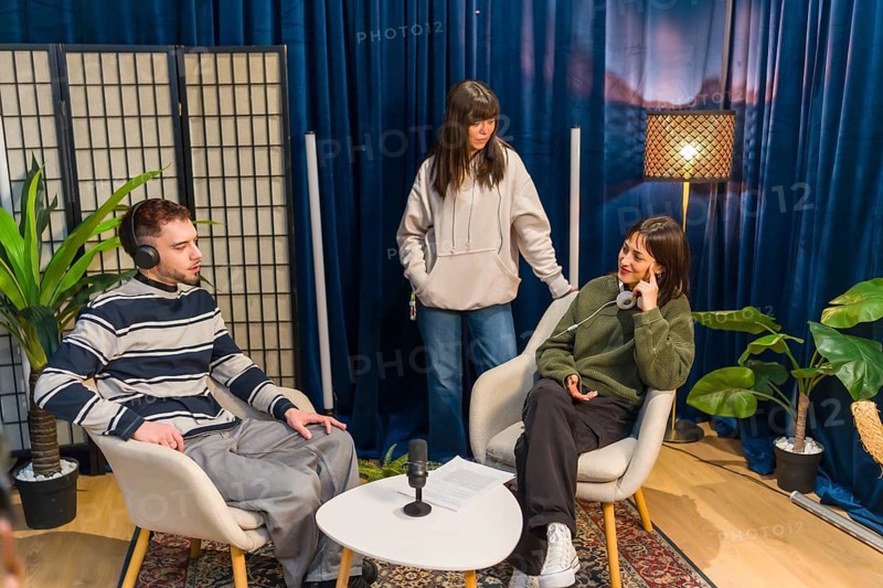 Three young people collaborating in a modern studio setup, creating audio content for a podcast or social media, utilizing microphones and headphones for engaging discussions