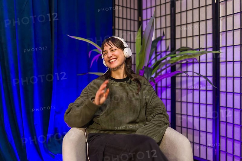 Young woman wearing headphones and smiling, actively engaging in content creation during a podcast audio recording or social media streaming session in a studio