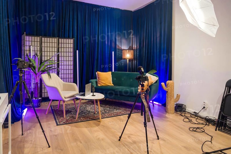 Modern content creation studio set up for video recording and podcast production, featuring cameras, microphones, lighting, and a comfortable seating area against blue curtains