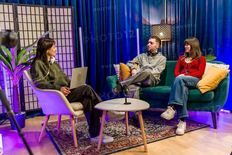 Young men and women are collaborating and talking in a colorful studio setting, recording a podcast or social media content using professional equipment