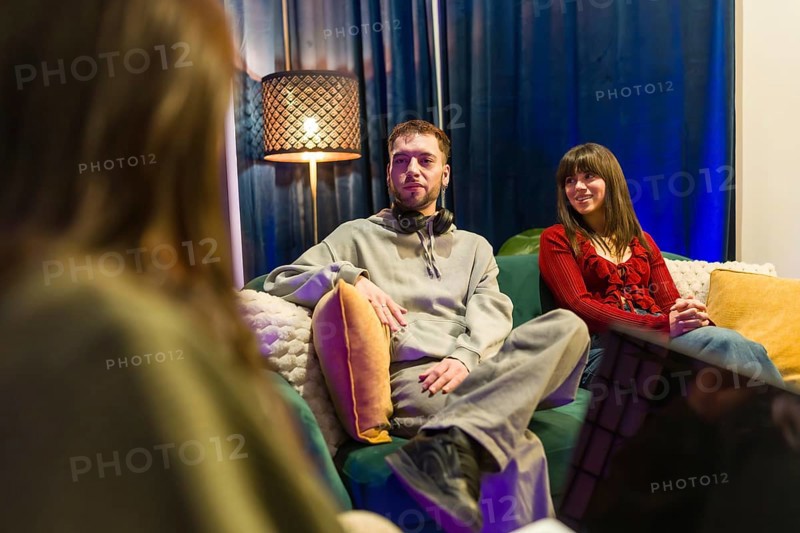 Young adults sitting on a sofa in a modern social media studio, interviewing guests and recording a podcast for online platforms and digital content, creating engaging multimedia