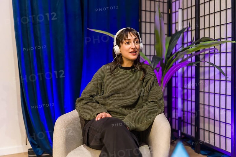 Young woman in a modern home studio wearing headphones, hosting a podcast or livestream, speaking into a mic while recording audio and engaging an online audience