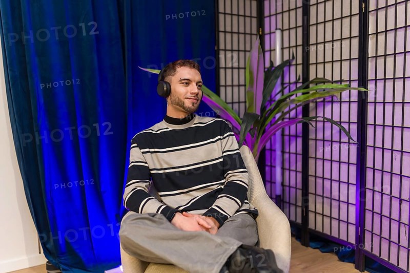 Young content creator wearing headphones, sitting in a modern studio setup, preparing for a podcast recording session or producing social media video material
