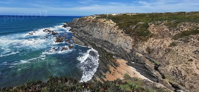 Coastal landscape with eroded rock formations and breaking waves on a sandy beach, hiking on the Fisherman's Trail, Algarve, Portugal