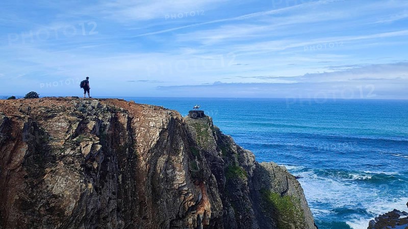 Lone hiker on rocky cliff overlooking the vast ocean, stork's nest (ciconia), Fisherman's trail, Algarve, Portugal