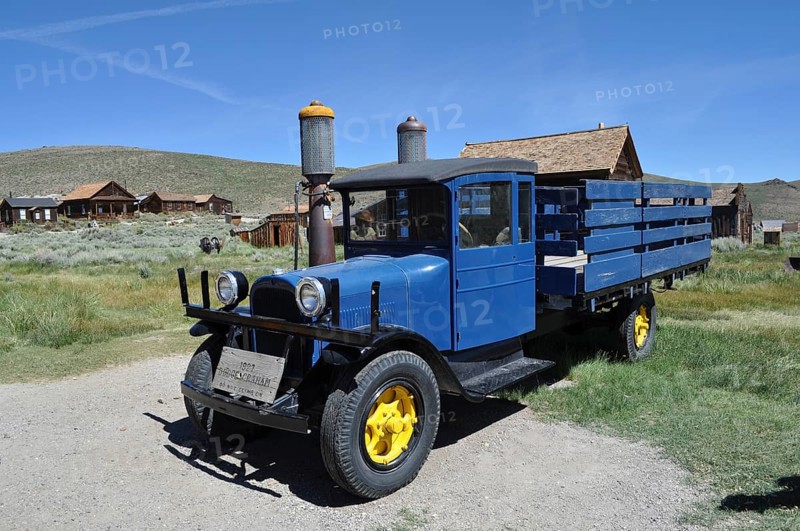 A blue historic truck with yellow wheels, Dodge Graham 1927, stands in front of a wooden house village in rural surroundings, Bodie Ghost Town, California, USA