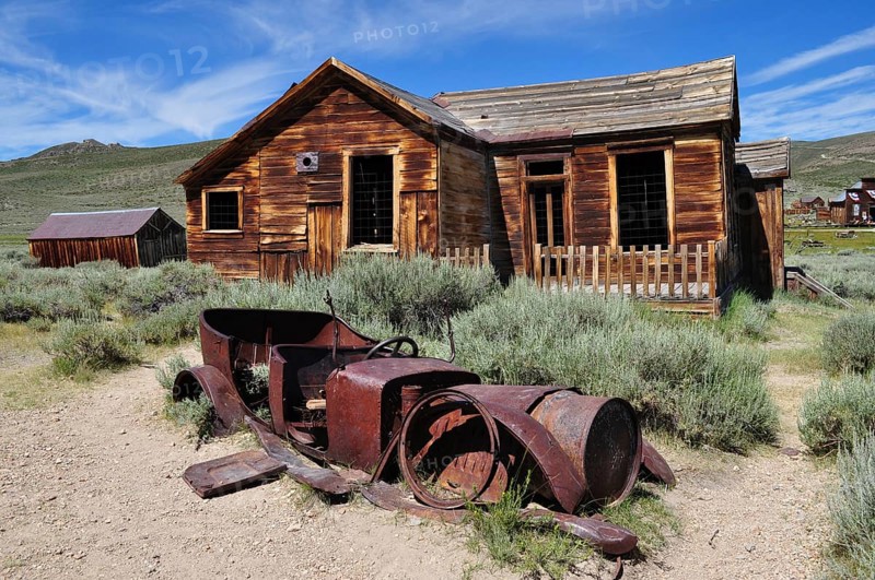 Old wooden house with rusty car wreck in front of it, surrounded by nature, Bodie Ghost Town, California, USA
