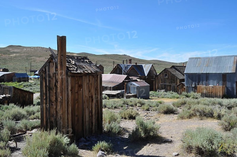 An abandoned village with several wooden houses, toilet, outhouse in the foreground, in a natural, rural area, Bodie ghost town, California, USA