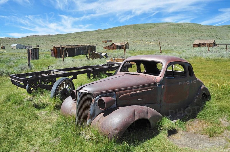 Rusty car wreck, Chevrolet Coupé, in front of historic buildings in natural setting, Bodie Ghost Town, California, USA