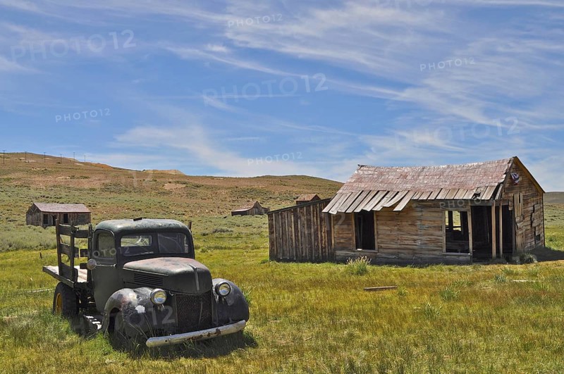 An abandoned car, vintage Ford Model 51 pickup truck, stands next to an old wooden cabin in a barren, rural landscape, Bodie Ghost Town, California, USA