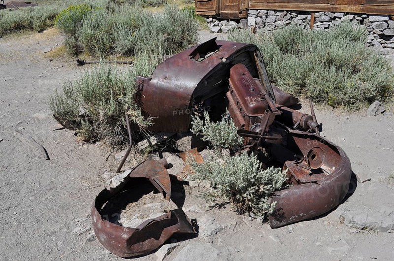 Old crumbling car wreck in a dry landscape with plants, Bodie Ghost Town, California, USA