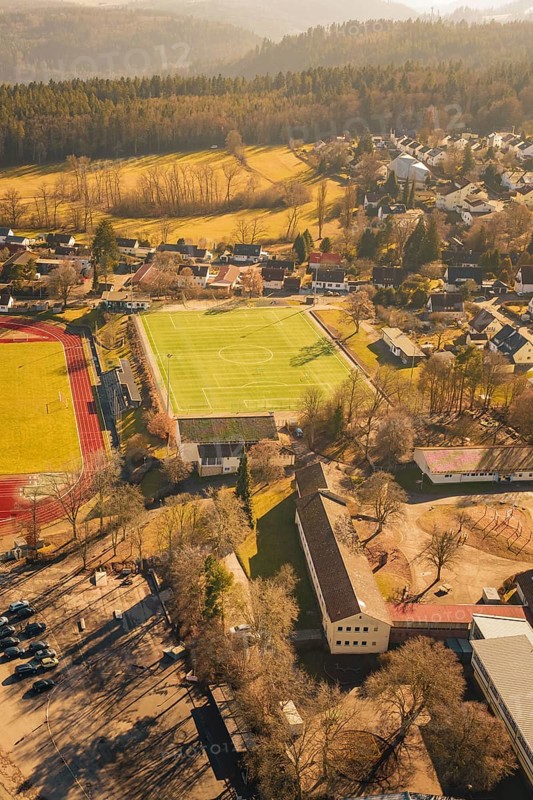 Residential area with sports ground and lots of trees in sunlight taken from the air, Wimberg, Calw, Germany