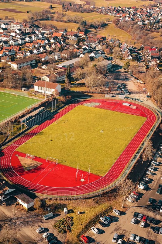 Sports field with red track and surrounding urban area seen from the air, Wimberg, Calw, Germany