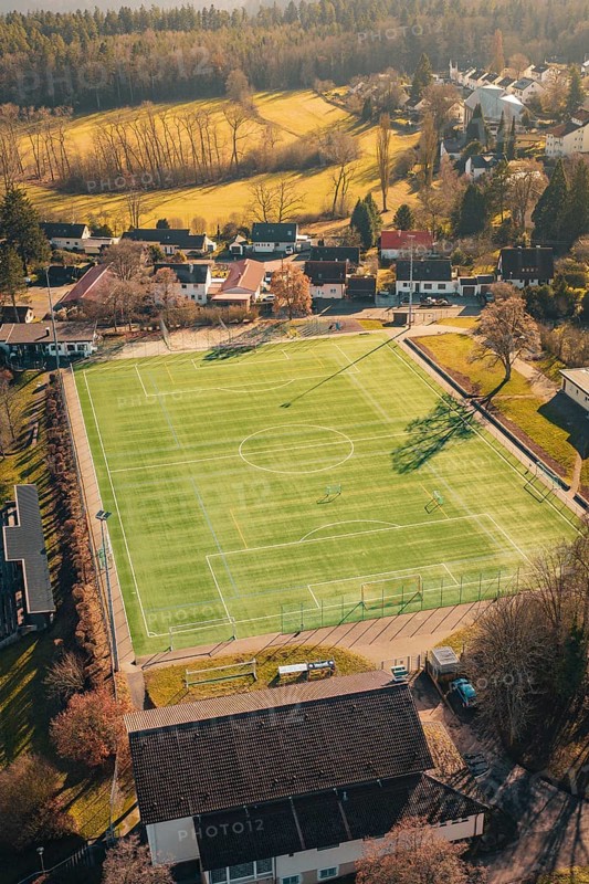 Green soccer field in rural area with surrounding trees and buildings, seen from the air, Wimberg, Calw, Germany