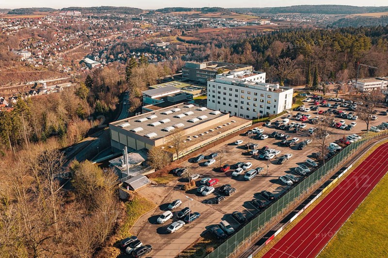 School with parking lot and several cars in a winter landscape with city and hills in the background, Wimberg, Calw, Germany