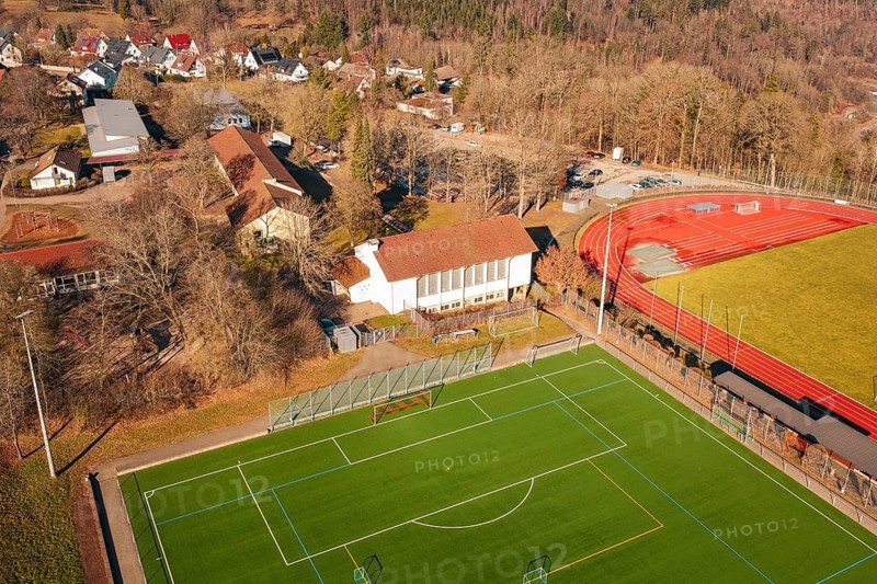 Aerial view of a sports field with red running track and nearby buildings in a village, Wimberg, Calw, Germany