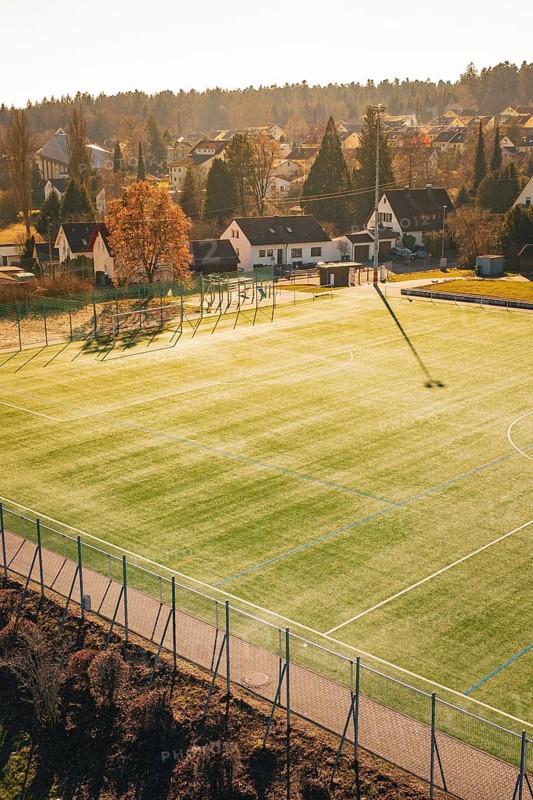Sunlight illuminates a soccer field in the village with houses and trees in the background, Wimberg, Calw, Germany