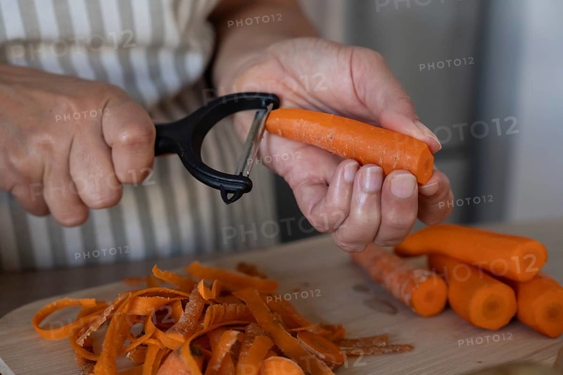 Close up of hands peeling fresh carrot on cutting board in modern kitchen. Simple ingredients, healthy cooking and everyday food preparation