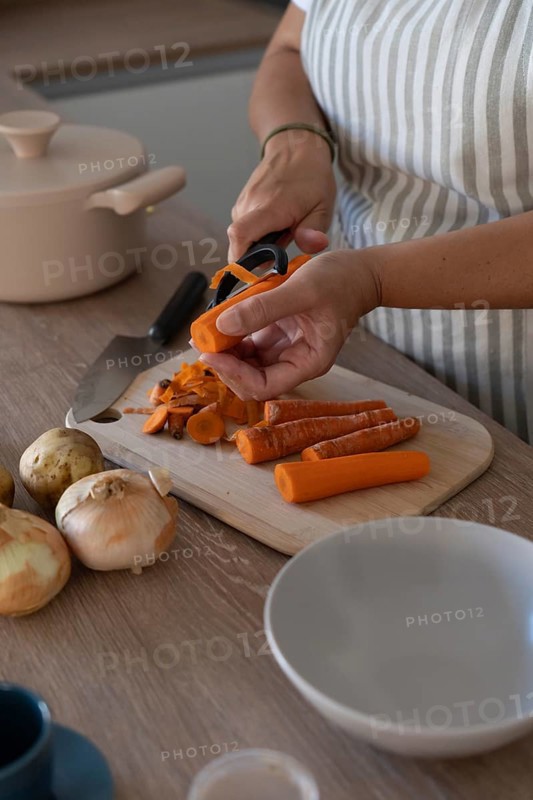 Vertical image of hands peeling carrot in modern kitchen. Casual home cooking, fresh ingredients and everyday routine
