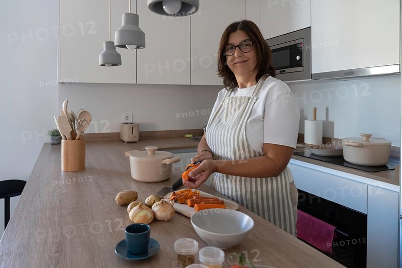 Woman preparing carrots, potatoes and onion for homemade soup in modern kitchen. Comfort food, simple ingredients and healthy cooking concept