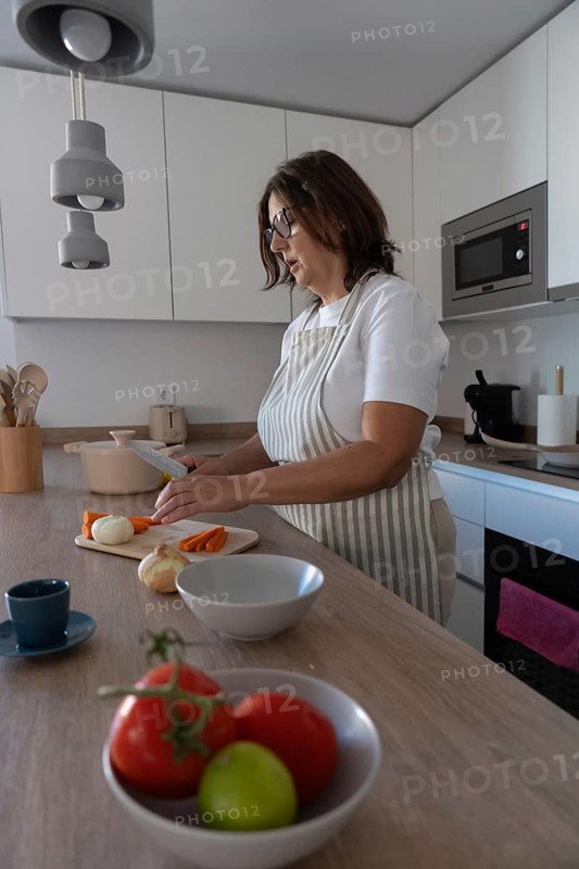 Woman cooking at home while cutting carrots on wooden cutting board. Everyday routine, homemade food and domestic lifestyle