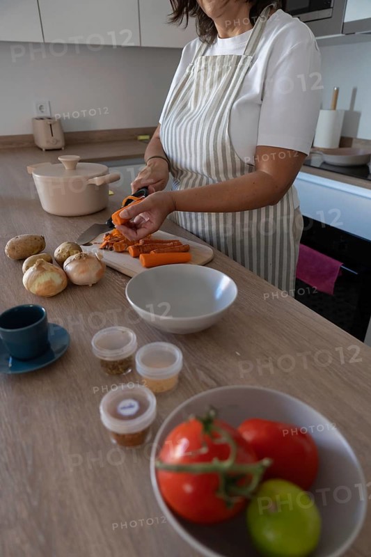 Vertical close up of hands peeling fresh carrot on cutting board in modern kitchen. Healthy cooking, simple ingredients and everyday home lifestyle with copy space
