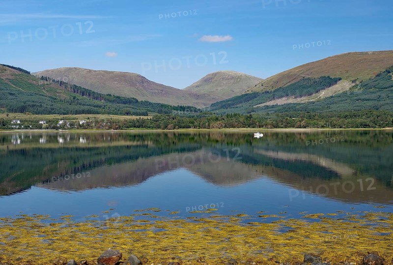 A calm body of water reflects the surrounding mountains and clear skies, Highlands, Fort William, Scotland, Great Britain