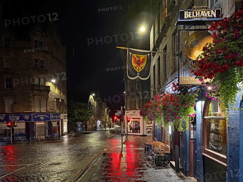 Night view of a quiet city street with wet pavement and illuminated shops. Royal Mile, Edinburgh, Scotland, United Kingdom