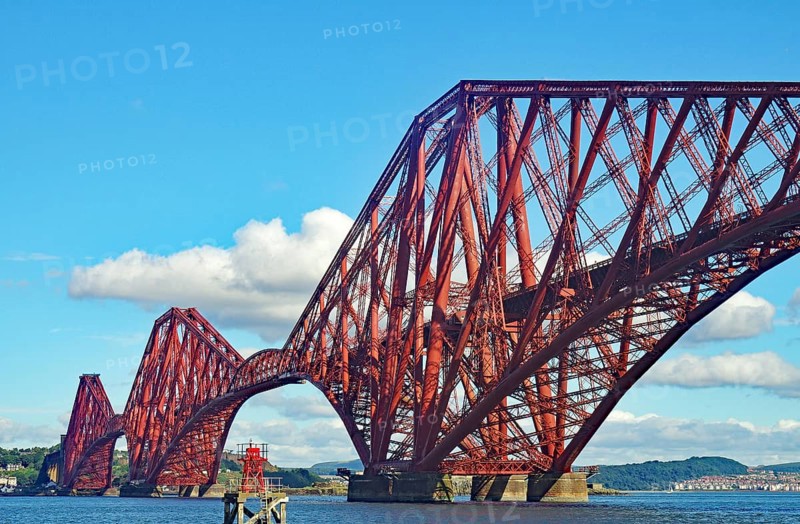 Large red metal bridge against a blue sky with white clouds, railway bridge across the Firth of Fourth, Edinburgh, Scotland, United Kingdom