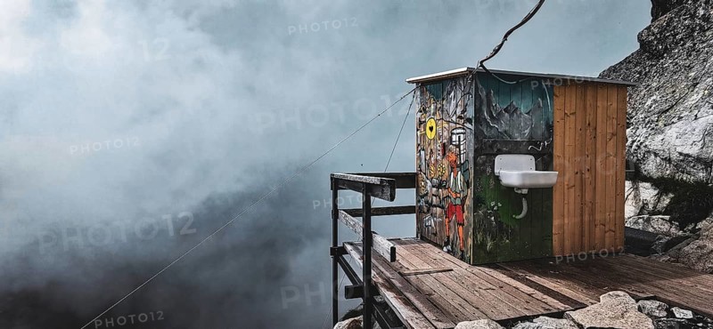 Colourful toilet at the Chata pod Rysmi mountain hut on a wooden platform in the middle of a mountainous, foggy landscape with wall art, graffiti, hiking, climbing Rysy, High Tatras, Slovakia