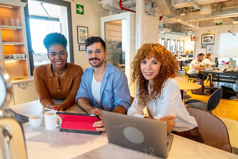 Diverse team of business professionals smiling while working together on projects and having a break in a bright, contemporary open plan coworking office space fostering teamwork