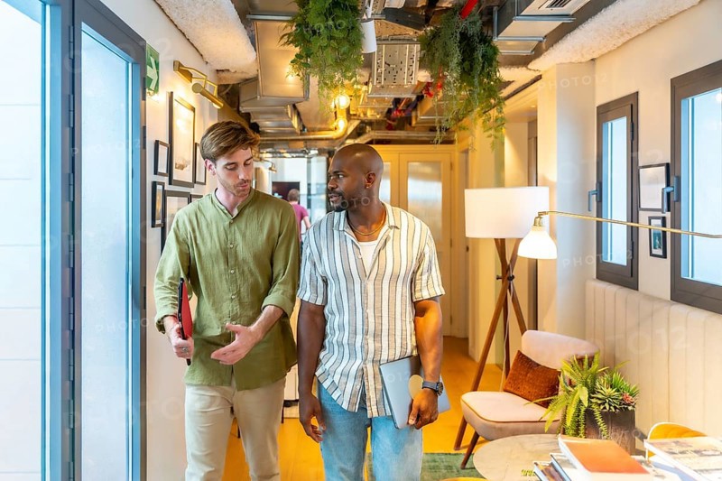 Two diverse colleagues walking and engaging in conversation while collaborating in a modern coworking office space during a break, reflecting teamwork and business communication