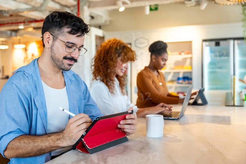 Diverse colleagues working on personal devices in a modern office, focusing on tasks and collaborating in a vibrant coworking space during a break or meeting