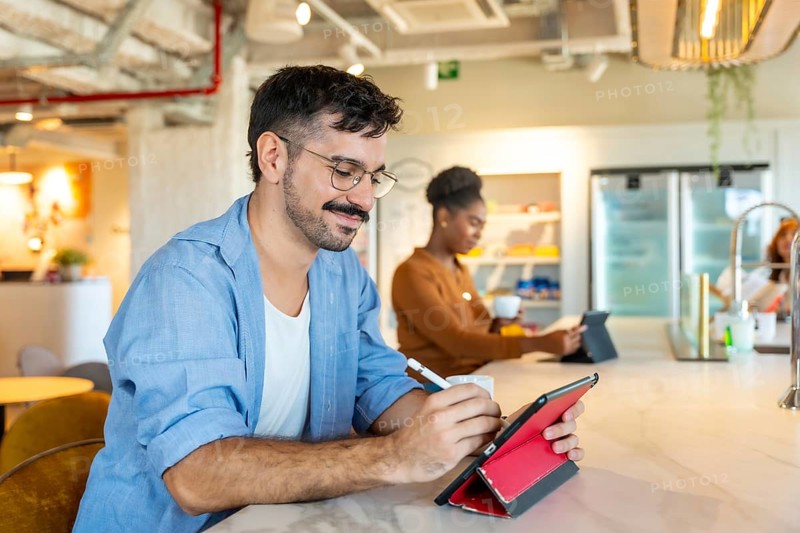 Diverse individuals making notes on a digital tablet and drinking coffee in a modern coworking space. Illustrating teamwork. Communication. And technological integration in a professional environment