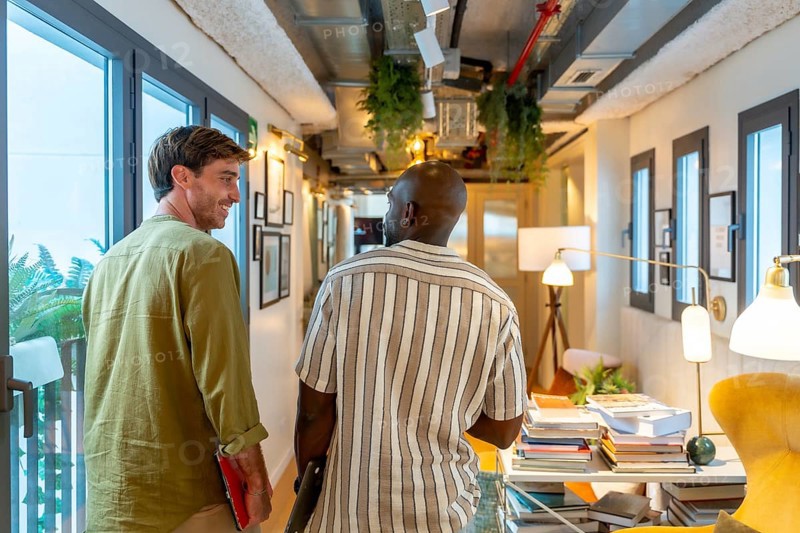 Two diverse colleagues walking and conversing in a modern office or coworking space, sharing ideas and collaborating during a break, depicting teamwork and professional interaction