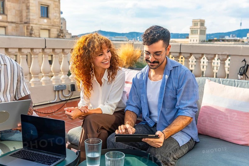 Two diverse colleagues collaborating during an outdoor business meeting on a professional coworking rooftop, using a laptop and tablet for teamwork and planning