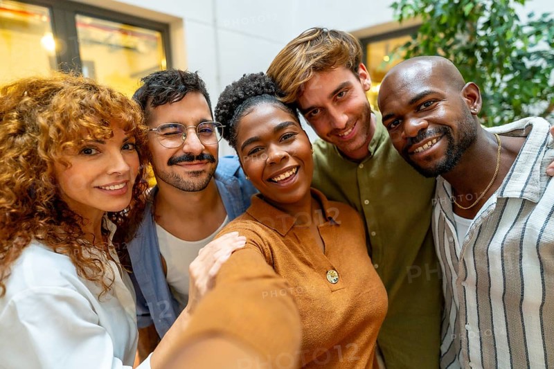 Diverse group of smiling business colleagues taking a cheerful selfie together, showing teamwork, friendship, and positive office culture in a modern coworking space