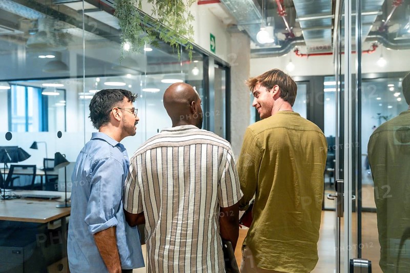 Three diverse men colleagues are engaging in conversation, networking, and discussing ideas while standing in a contemporary office or coworking space during a break