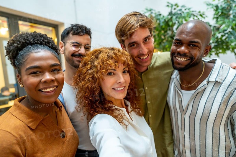 Diverse group of smiling business people looking at camera, capturing a self portrait together during a casual break from work in a bright, modern office or coworking space