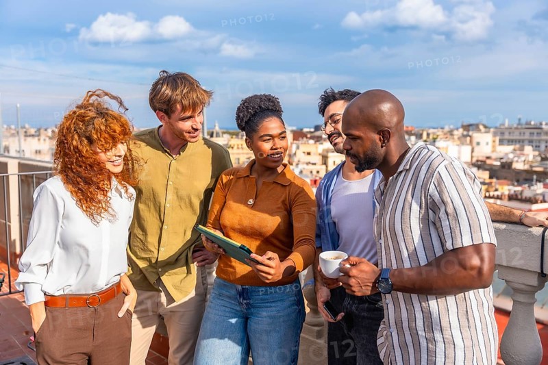 Diverse business people standing on a sunny urban rooftop, networking and collaborating while reviewing content on a digital tablet during a successful meeting