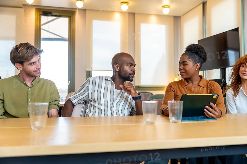 Diverse group of business colleagues engaging in a collaborative meeting, discussing ideas, and working together around a table in a modern coworking office space
