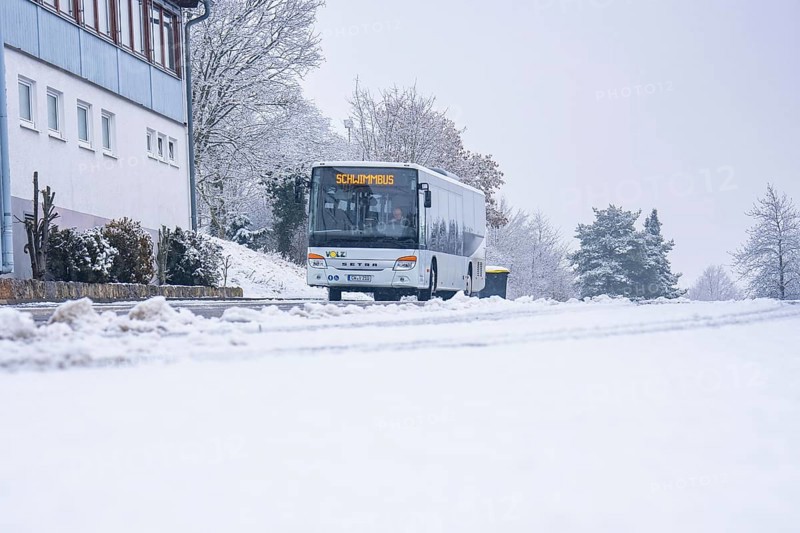 A bus travels on a snowy road surrounded by trees and buildings, Gechingen, Calw district, Germany
