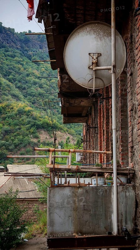 Old satellite dish on the balcony of a building with views of green mountains, Armenia