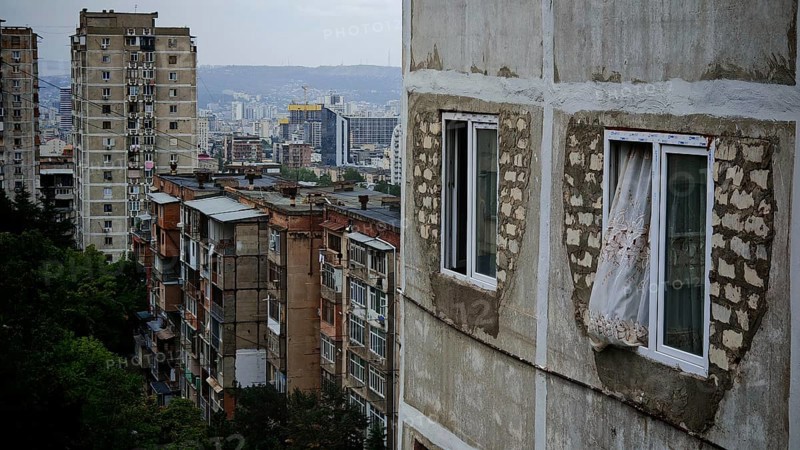 Old apartment blocks with worn facades against a city backdrop, nostalgic curtain blowing out the window, Tbilisi, Georgia