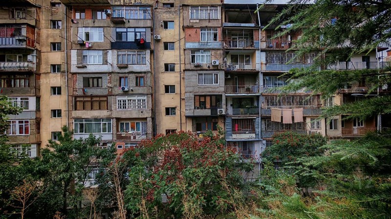 The entire façade of an old multi-storey residential building with many balconies and surrounded by trees, laundry drying on the balcony, interesting, nostalgic atmosphere, flair, Tbilisi, Georgia