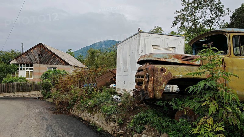 A rusty truck is parked in front of a small house on the side of the road in a village, retro charm, Armenia